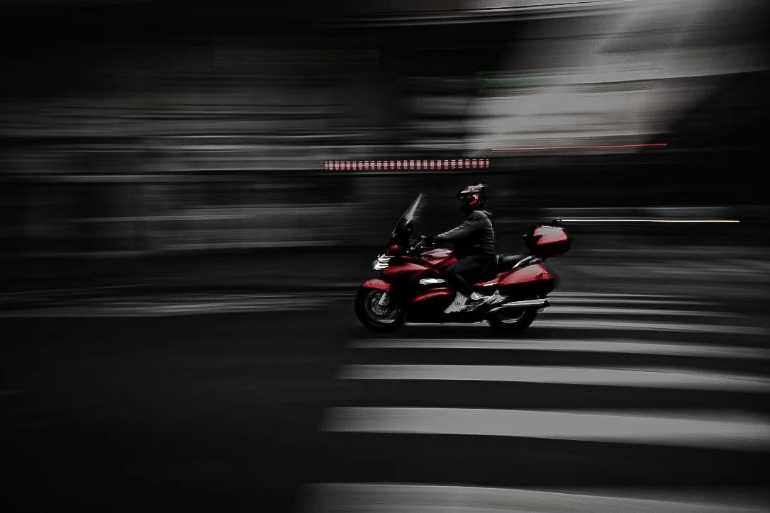 A person riding a red scooter on a city street at night, with motion blur background.