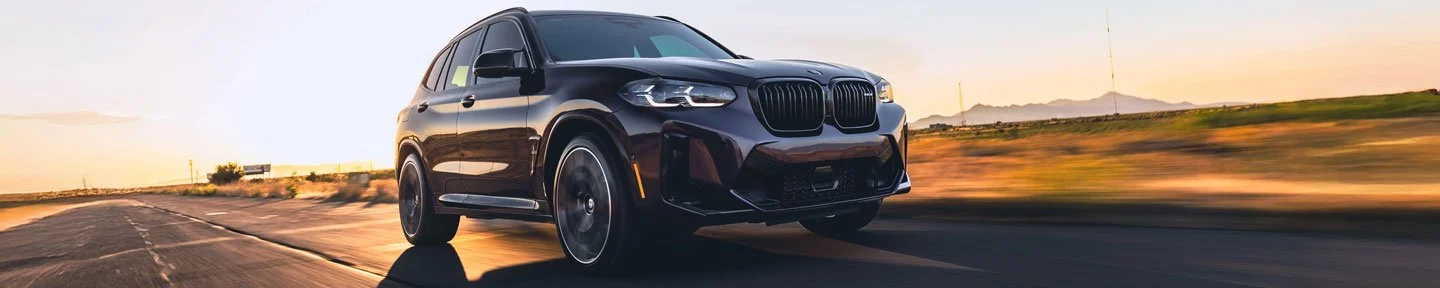 Black BMW SUV driving on an open road during sunset.