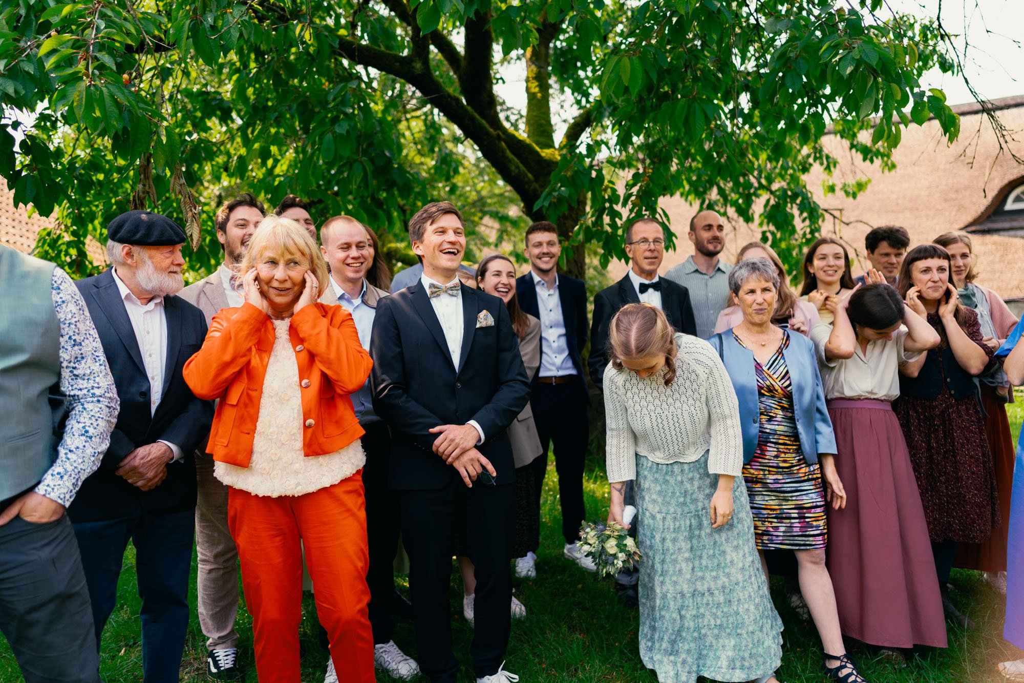 Gruppen von Menschen bei einer Hochzeit im Freien, lachend und fröhlich unter einem Baum.
