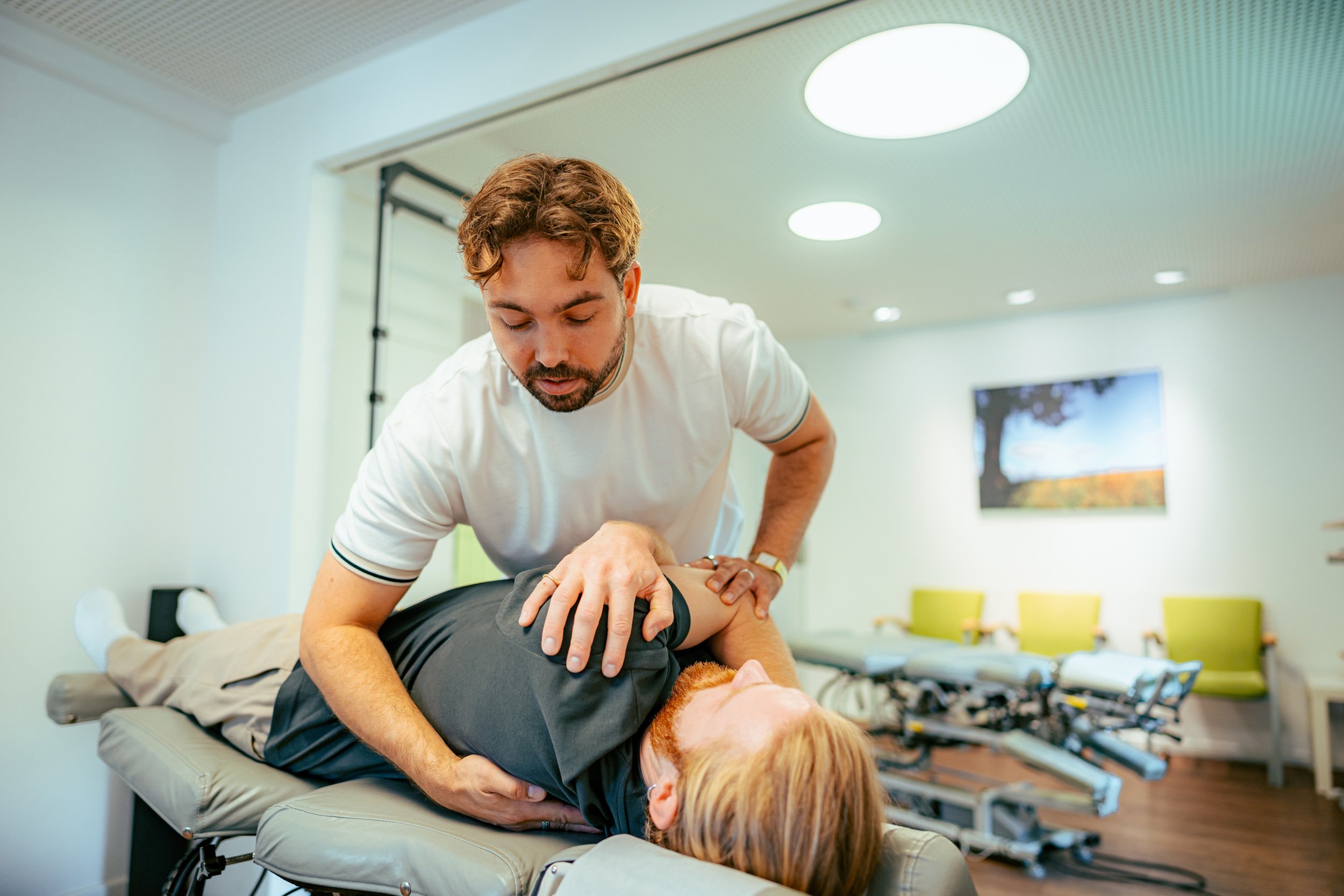 Ein Therapeut oder Physiotherapeut behandelt eine Patientin, die auf einer Behandlungsliege liegt, in einem freundlichen und modernen Rehabilitationszentrum oder Physiotherapie-Praxis.