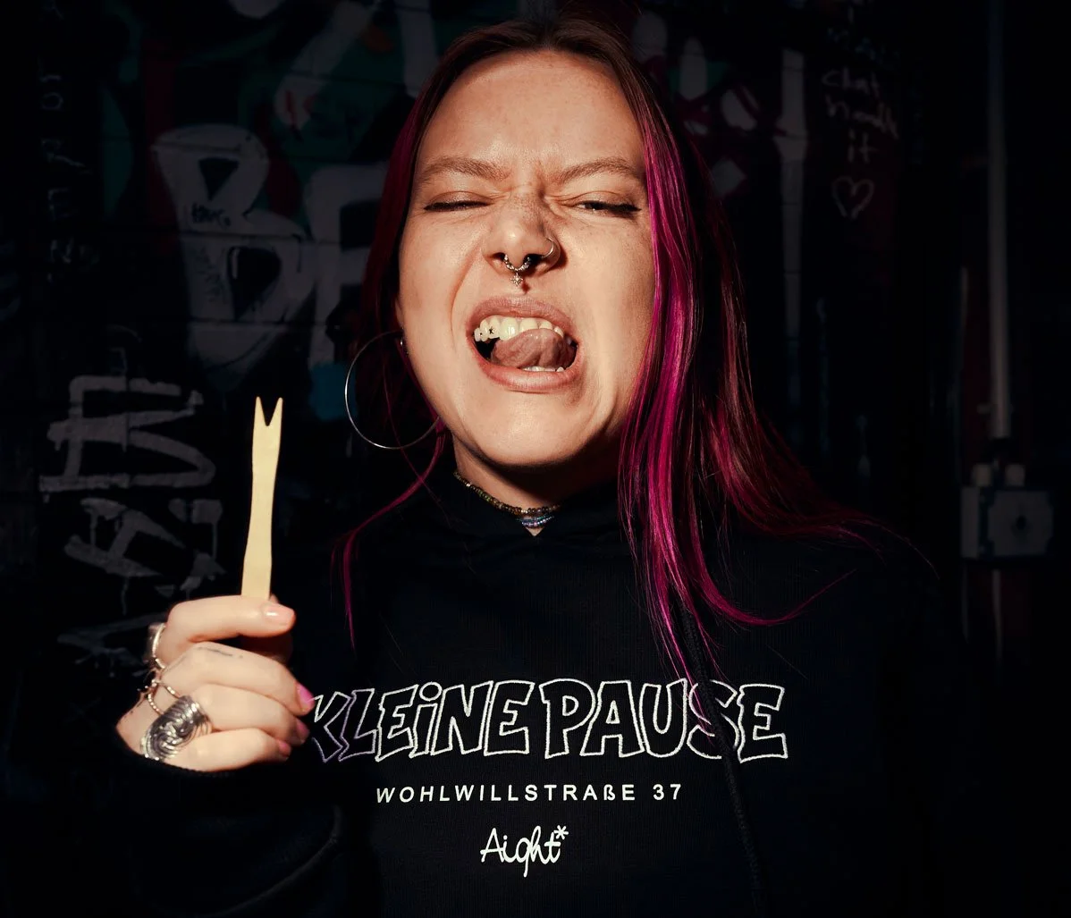 Eine junge Frau mit pinkfarbenen Haaren, tätowiertem Gesicht und Nasenpiercing, die wütend aussieht, während sie eine Holzschweden in der Hand hält.