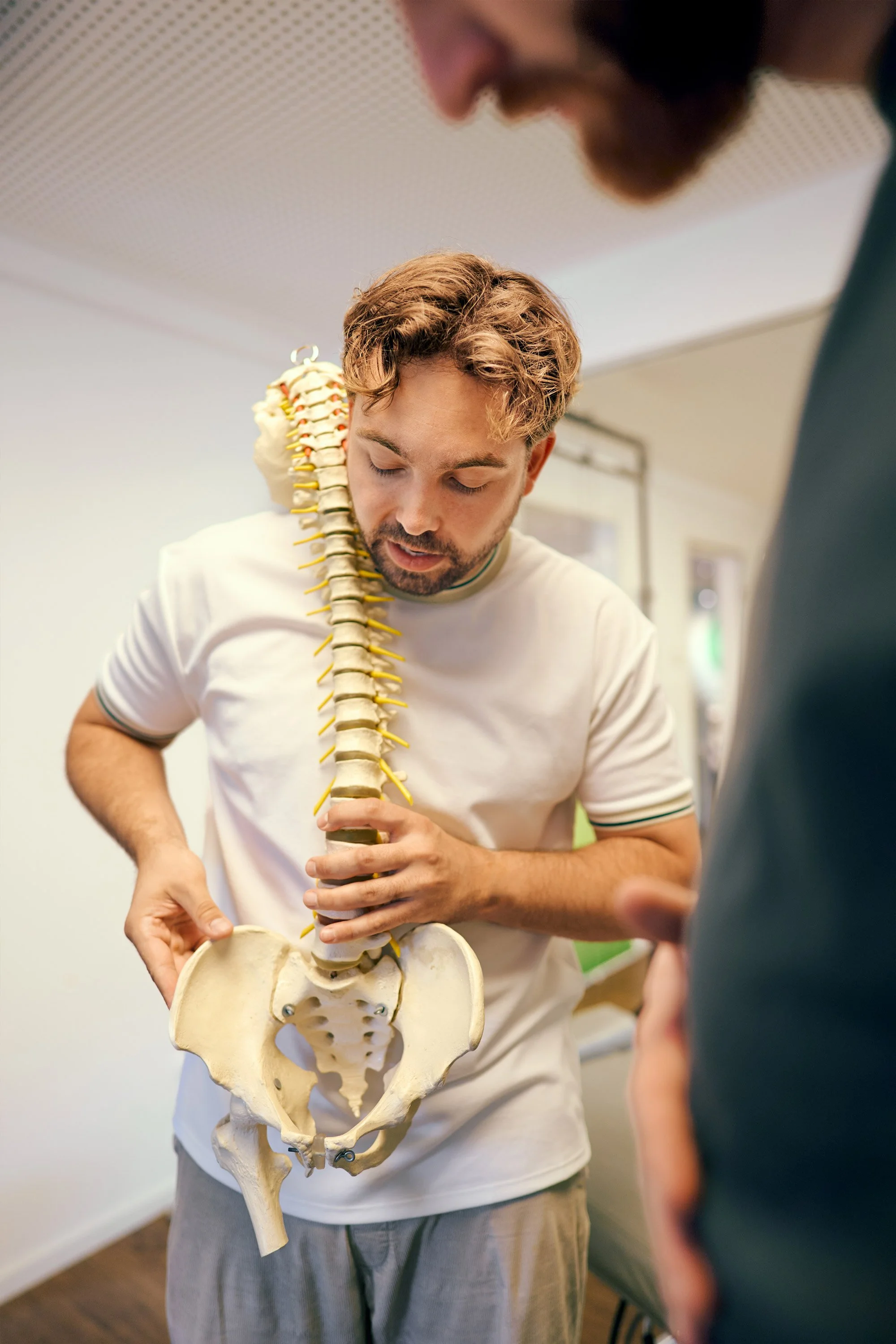 Ein Mann erklärt an einem Knochenmodell der menschlichen Wirbelsäule und des Beckens auf einem medizinischen Ausbildungsraum.