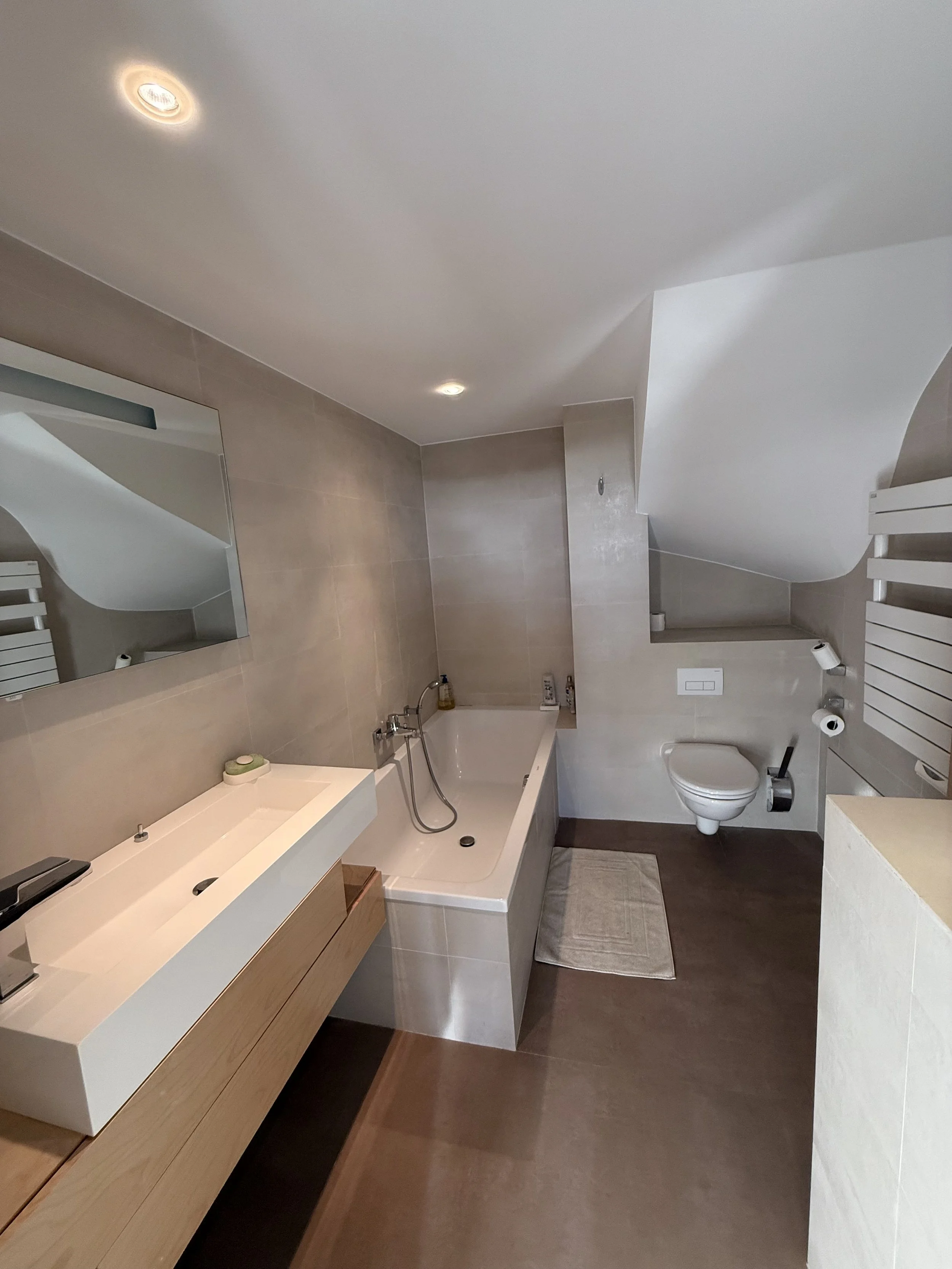Salle de bain moderne avec douche, baignoire, lavabo, miroir et toilettes dans une décoration élégante et minimaliste.