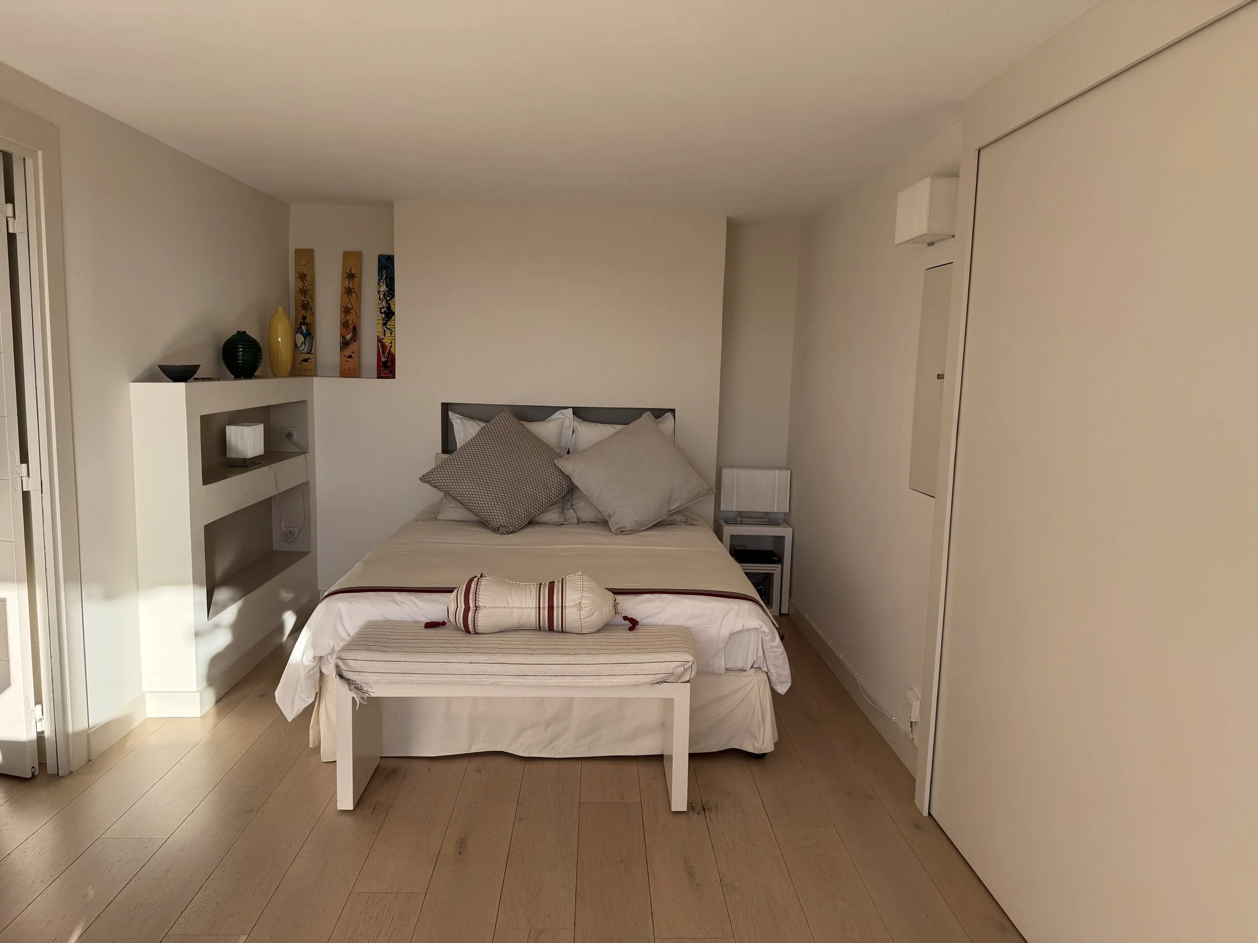 Chambre avec lit simple, oreillers, petite table de nuit, décor coloré et étagères.