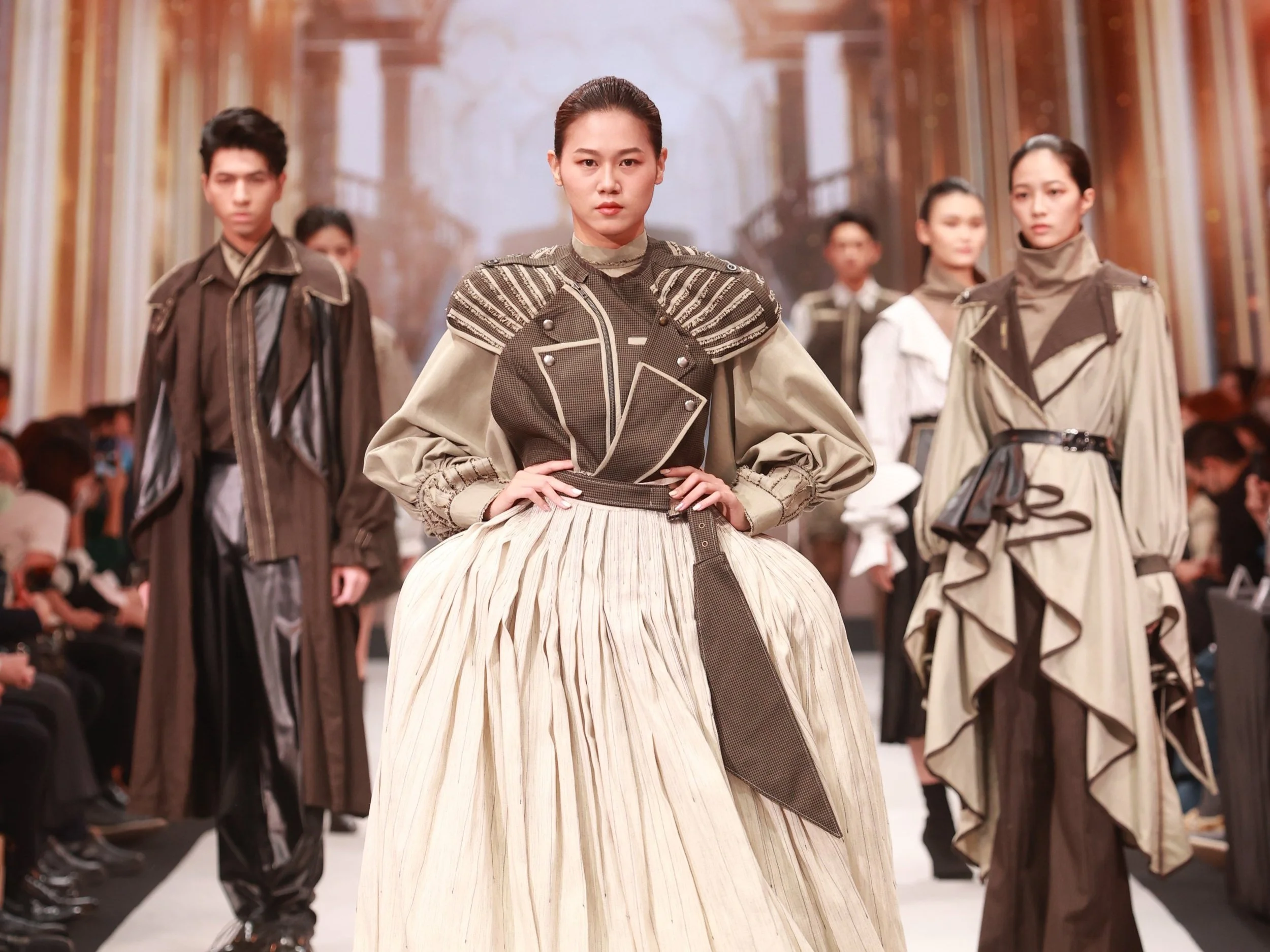 Models walking on a runway with elaborate, fashion-forward outfits in an indoor setting.