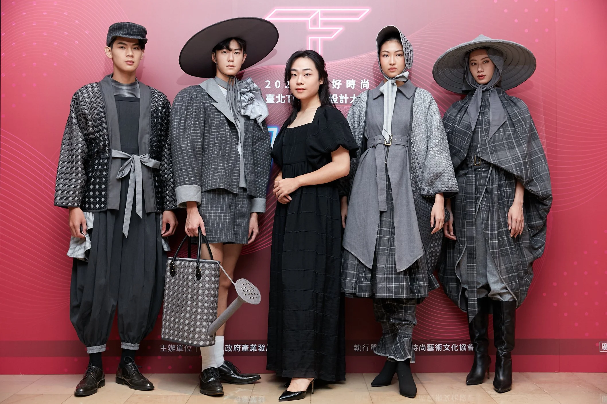 Group of five young adults dressed in fashionable, traditional-inspired clothing, standing in front of a pink background with stylized designs and Asian characters.
