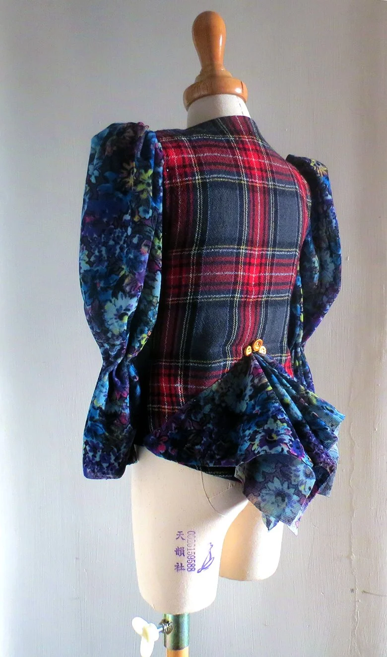 A dress form wearing a jacket with a tartan pattern on the back and floral fabric sleeves and bow detail.