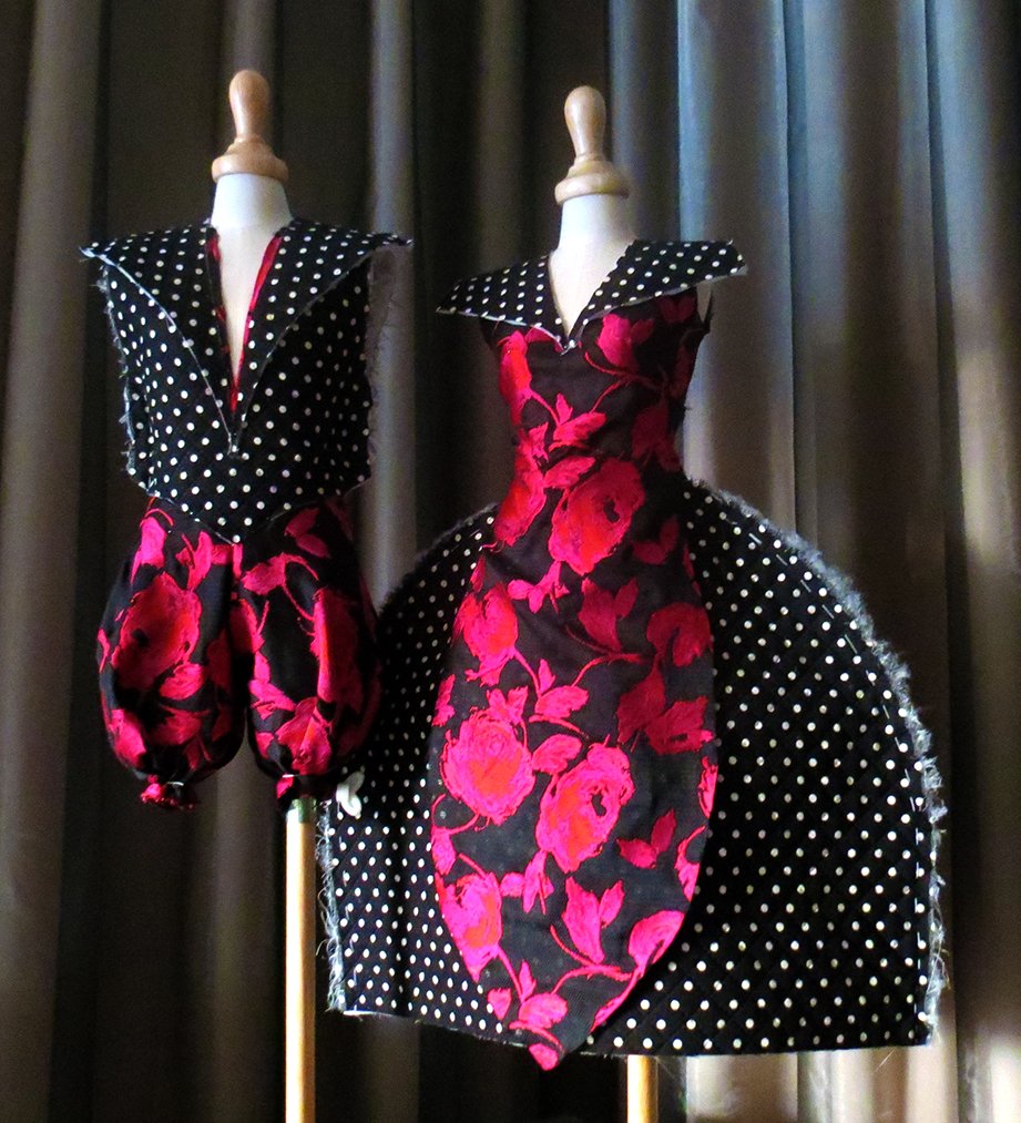 Two mannequins dressed in vintage-style black and red polka dot and floral dresses, set against dark curtains.