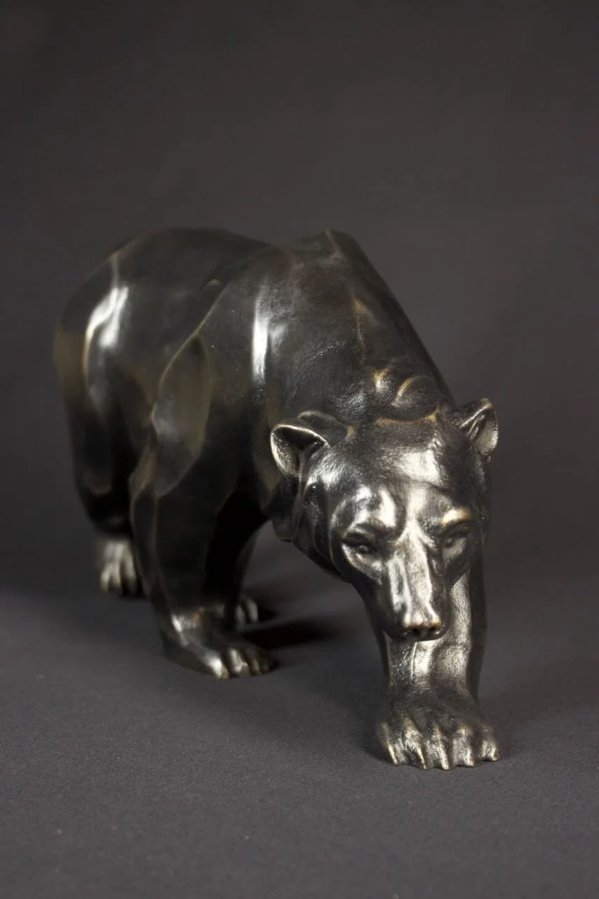 A dark metallic Brother (bronze) bear sculpture walks forward, set against a plain dark background.