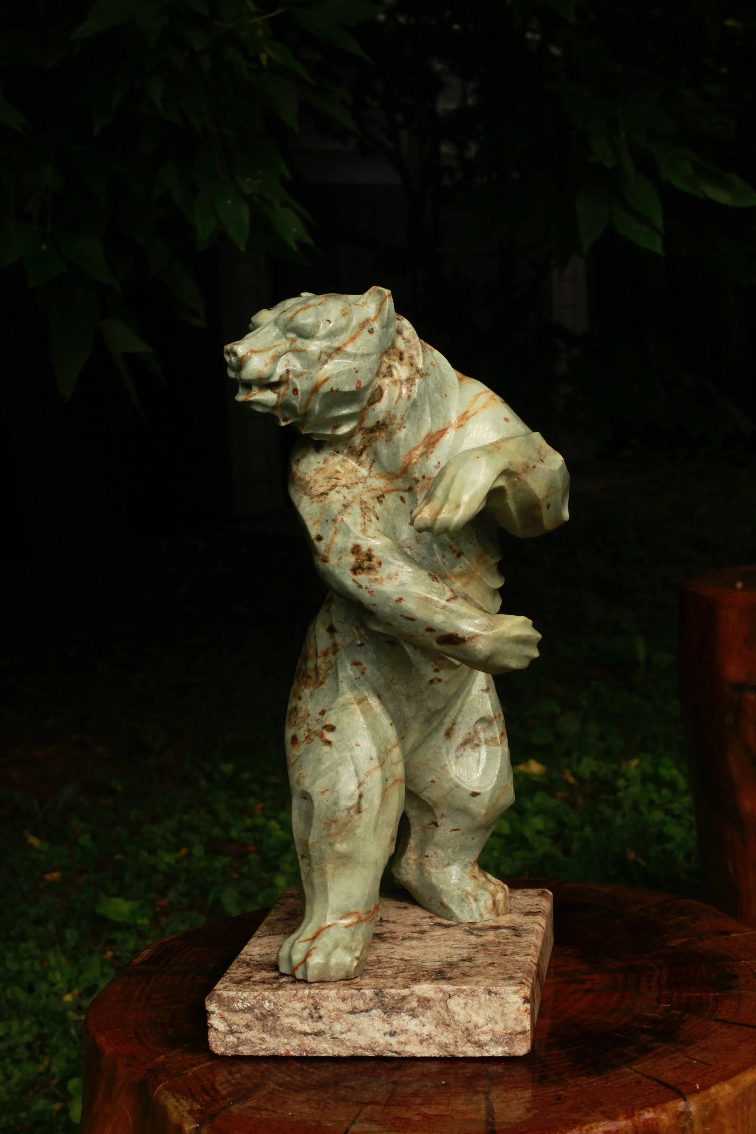 Soapstone sculpture of a bear standing on its hind legs on a stone surface outdoors.