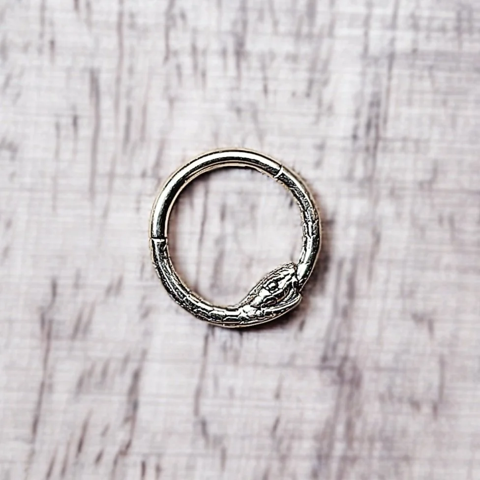 Gold-tone Ouroboros clicker ring shaped like a snake eating its tail, with detailed scales and a polished finish; suitable for septum or daith piercings.