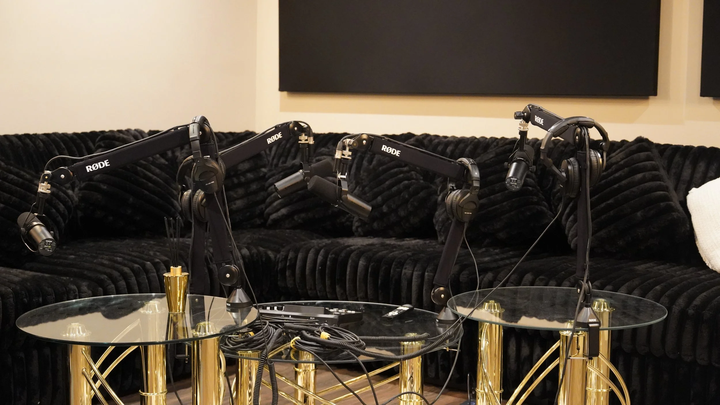 Recording studio setup with three microphones and headphones on a black velvet couch with glass tables.