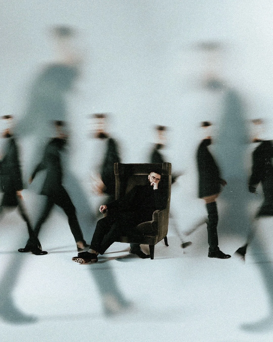 A person sitting in a large armchair surrounded by blurred walking people.