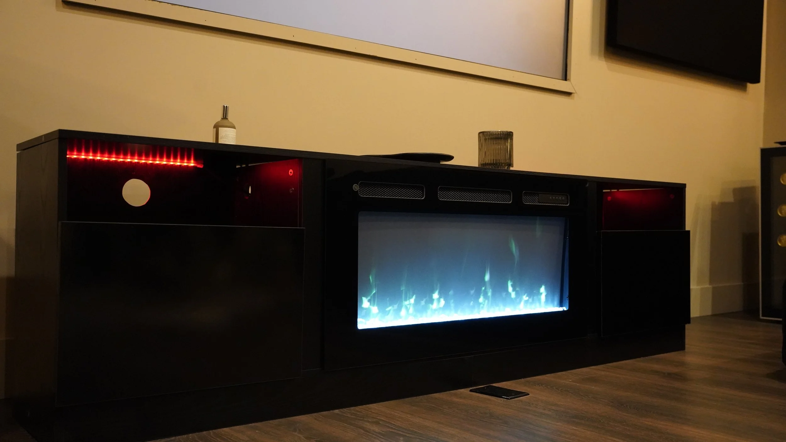 Modern black entertainment center with an electric fireplace, a candle, and a bottle of lotion on top.