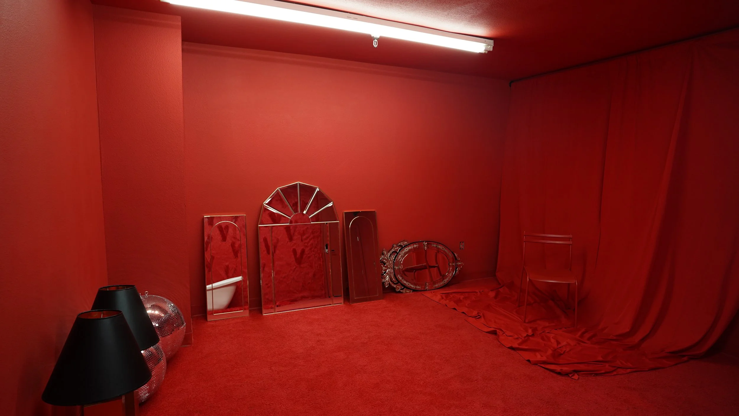 A room with red walls, carpet, and curtains. Contains black lamps, disco balls, and decorative mirrors leaning against the wall.