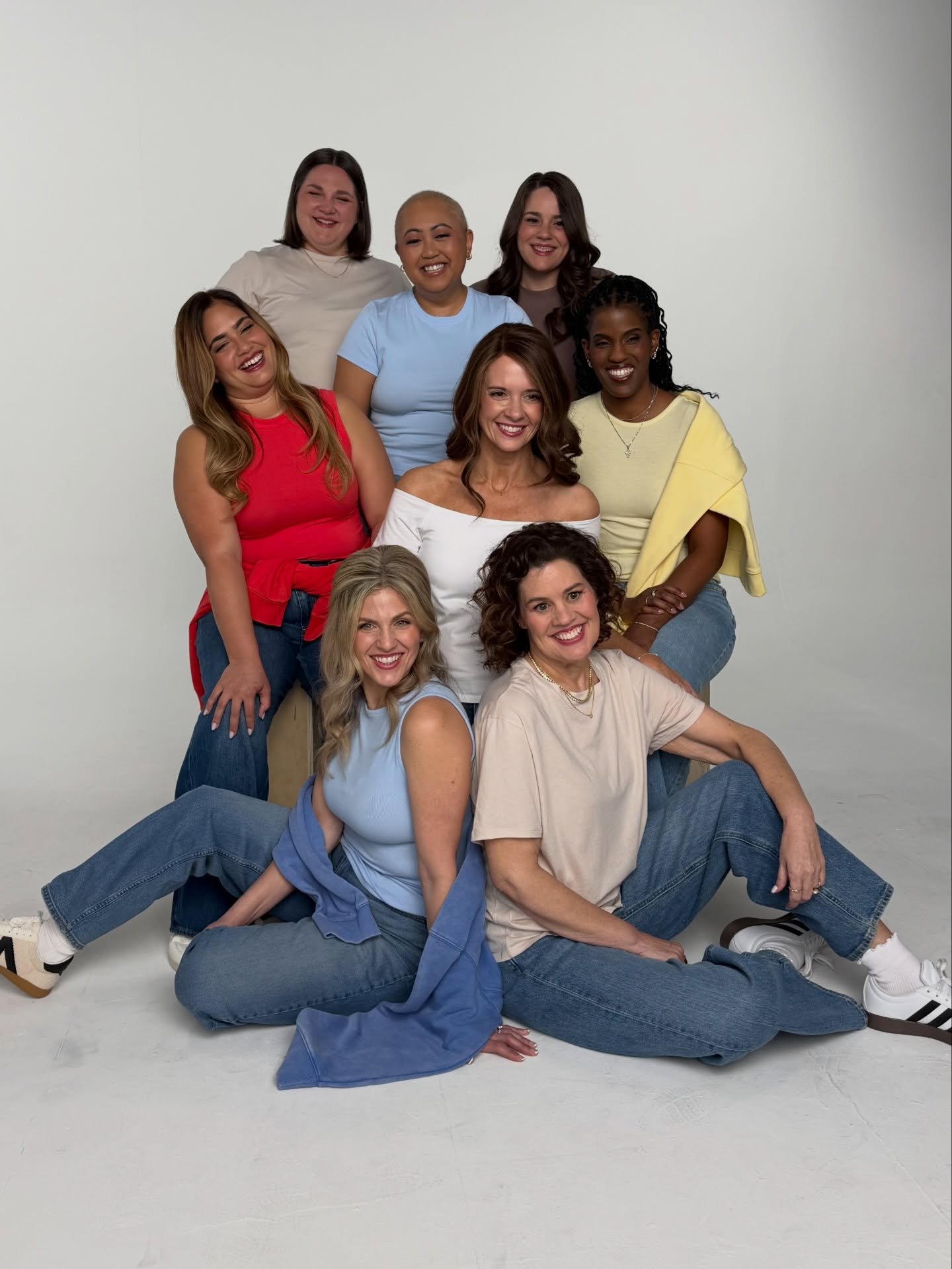 Group of nine diverse women smiling and posing together in a studio with a white background.