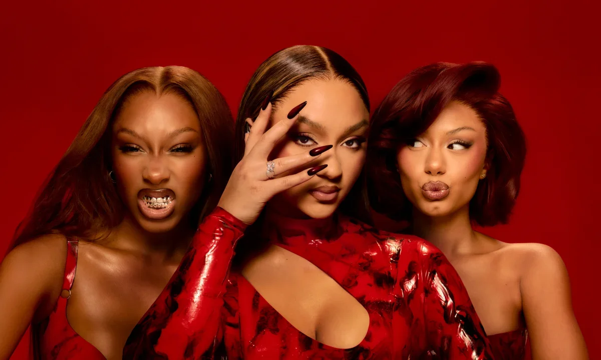 Three women with bold makeup and fashionable hairstyles posing against a red background.