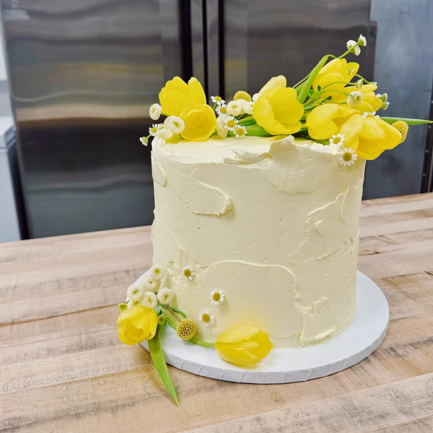 Cake of the Day: a cheerful butter-yellow birthday cake in our Strawberries and Cream flavor. This butter sponge cake with vanilla buttercream and fresh strawberries layered in between was a delight to make with the beautiful tulips and chamomile we 