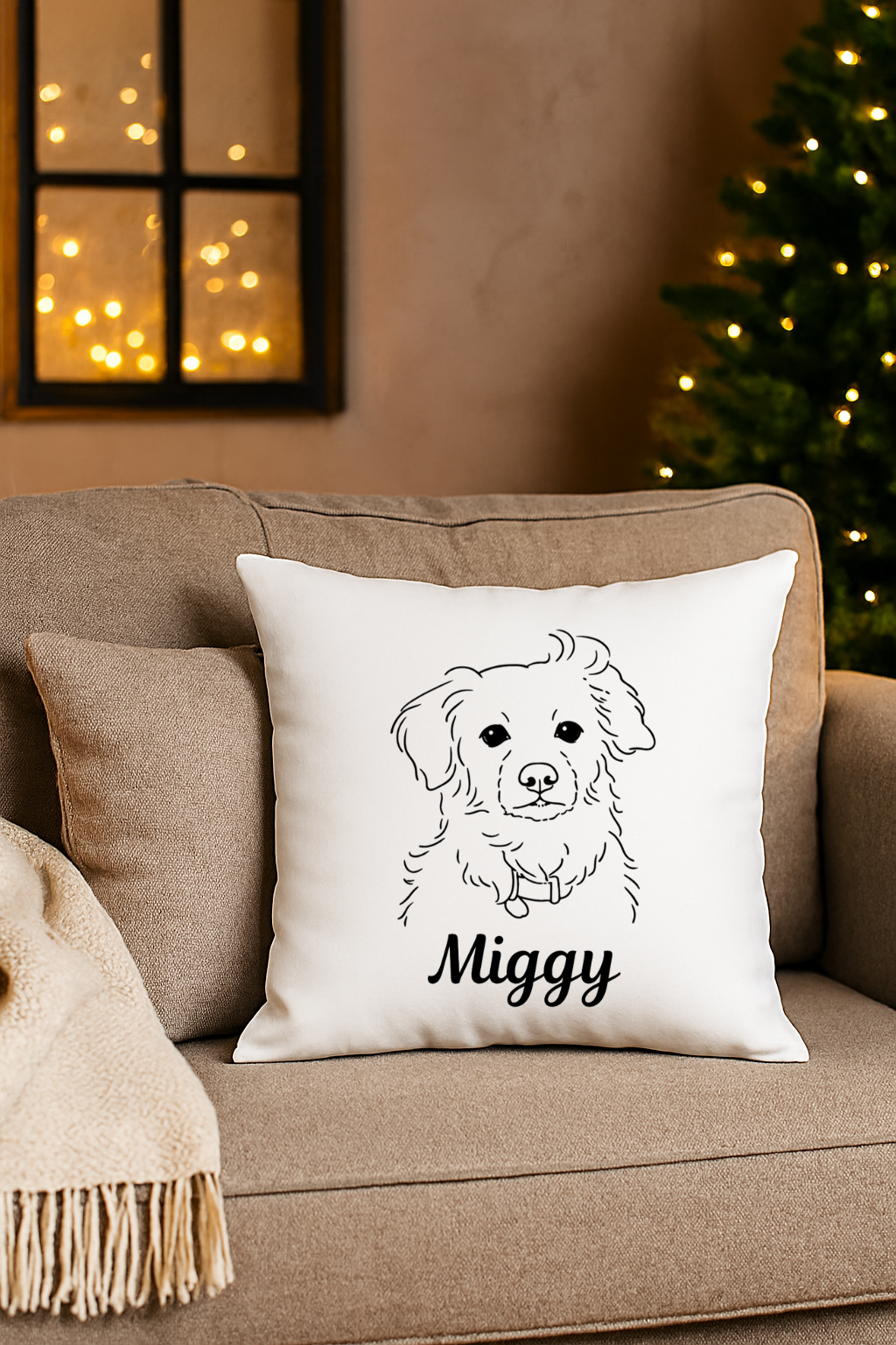 Decorative pillow on a beige sofa featuring a black outline drawing of a dog with the name "Miggy" written below, with a Christmas tree and window with fairy lights in the background.