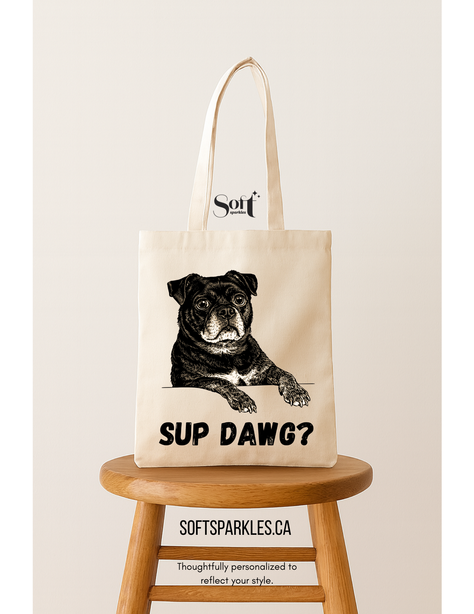 A beige tote bag featuring a black-and-white illustration of a dog with the words 'SUP DAWG?' printed below. The bag is placed on a wooden stool with a plain, off-white background.