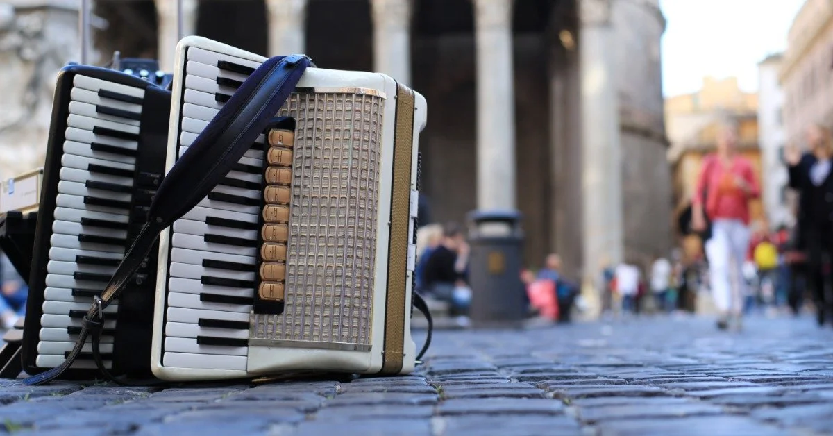 A red accordion and harmonica resting on cobblestone with the Pantheon’s columned facade in the background in Rome.