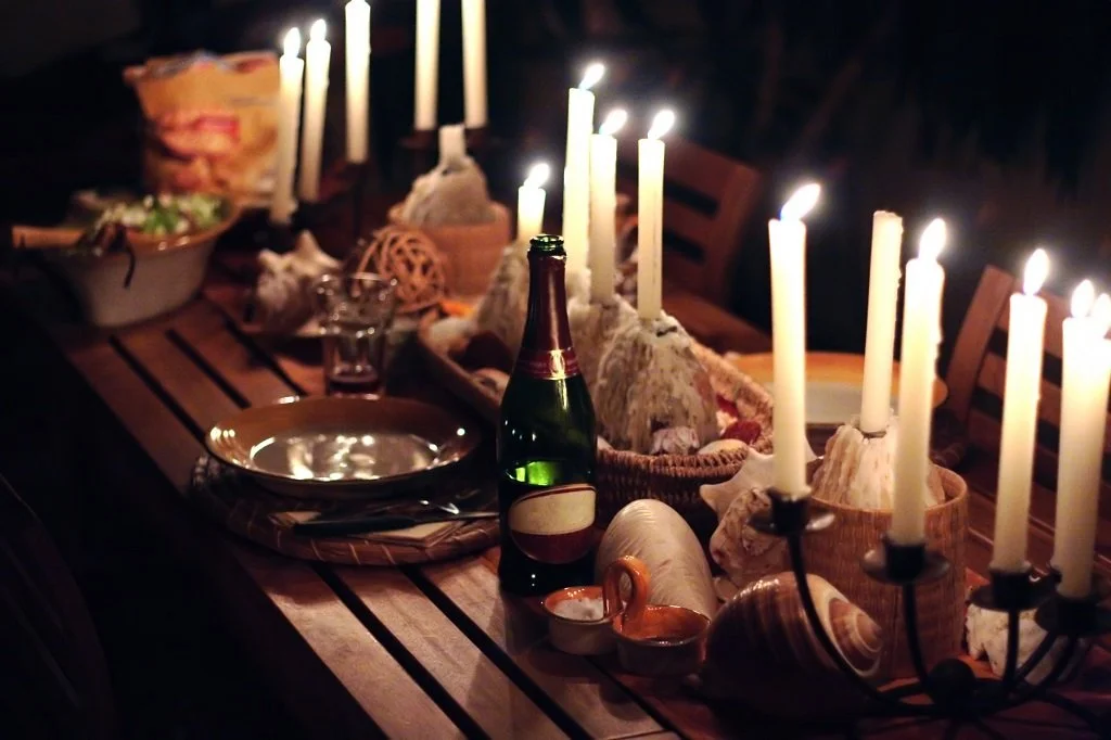 Table decorated with seashells, candles, and bottles, indicating a nighttime outdoor dinner setting, possibly for a special occasion.