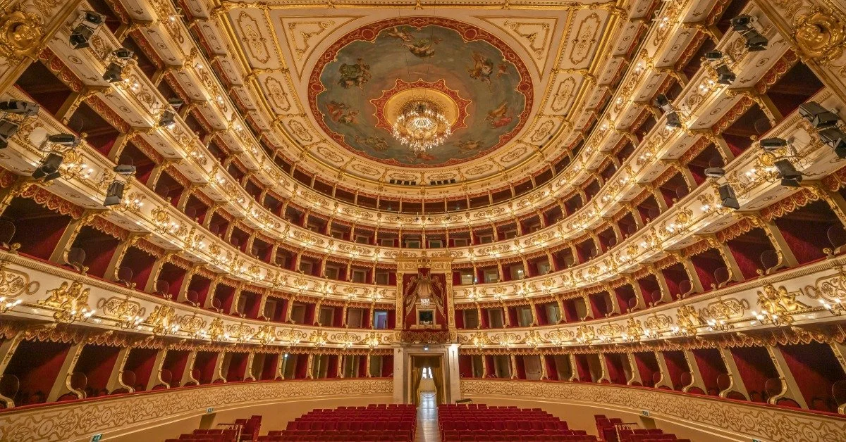 A panoramic view of a historic theater interior with rows of red seats, balconies, and decorative architectural details.
