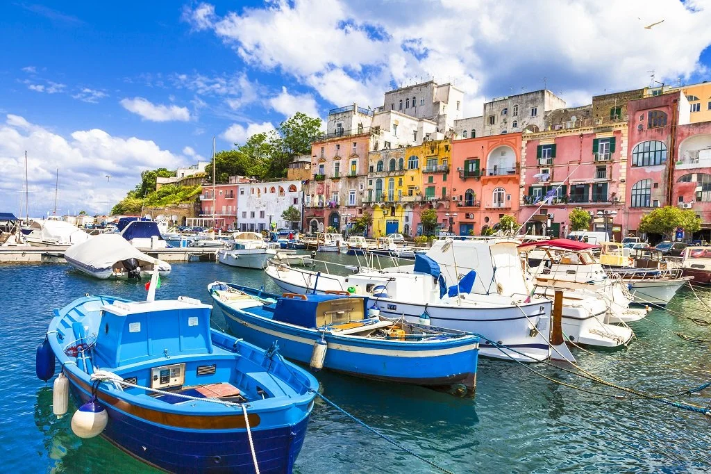 Colorful buildings overlooking a marina filled with boats and yachts under a blue sky with clouds.