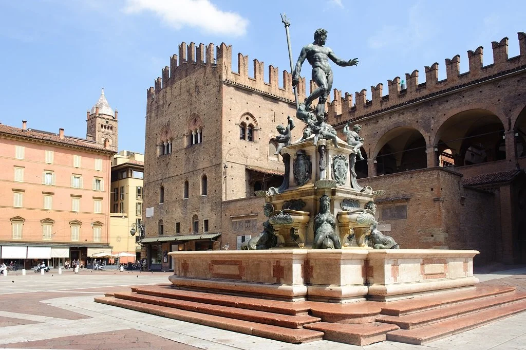 Statue of Neptune in a city square with historic brick buildings and a tower in the background.