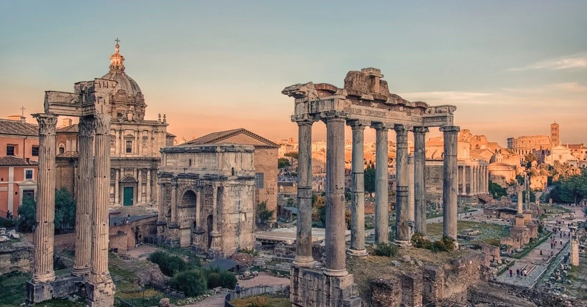 The Roman Forum at sunset, with ancient stone columns and ruins stretching across the historic center of Rome.