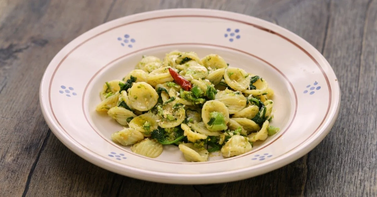 A bowl with a simple painted design filled with a serving of orecchiette con cime di rapa on a rustic wooden table.
