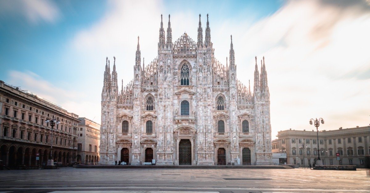 The Milan Cathedral rises over an open piazza, with its white marble facade glowing in soft morning light.