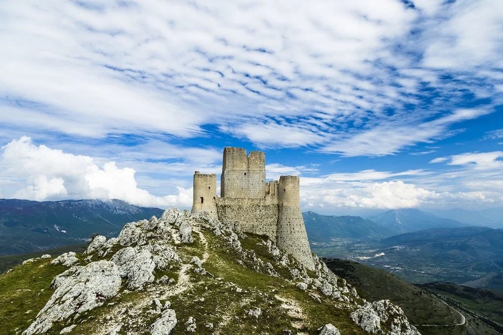Rocca Calascio, a medieval mountaintop fortress with a backdrop of surrounding mountains and blue sky, Abruzzo region.