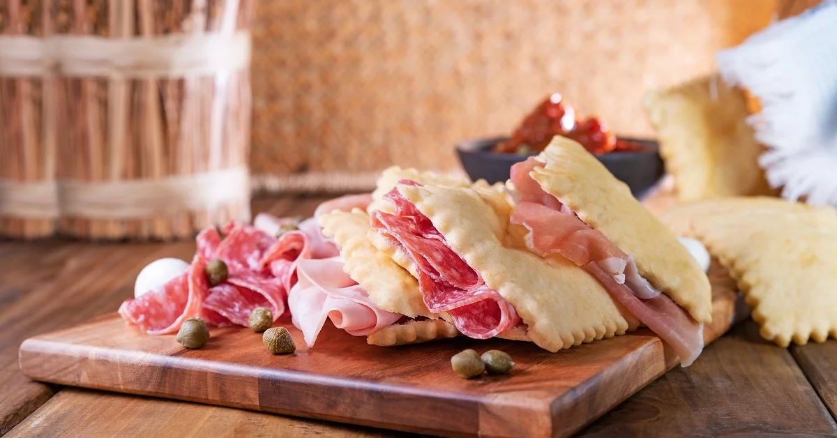 A close-up of a charcuterie board on a table in Northern Italy. The board features meat, cheese, and capers.