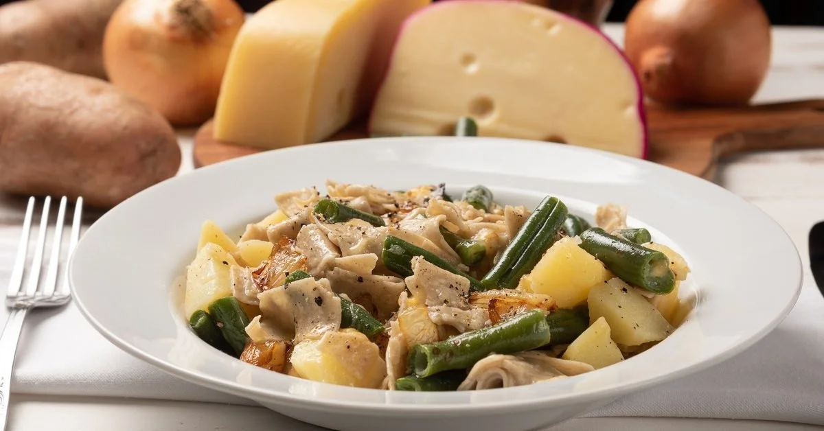 A close-up of a white dish with a Northern Italian pasta dish. The dish sits next to onions and cheese displayed on the table.