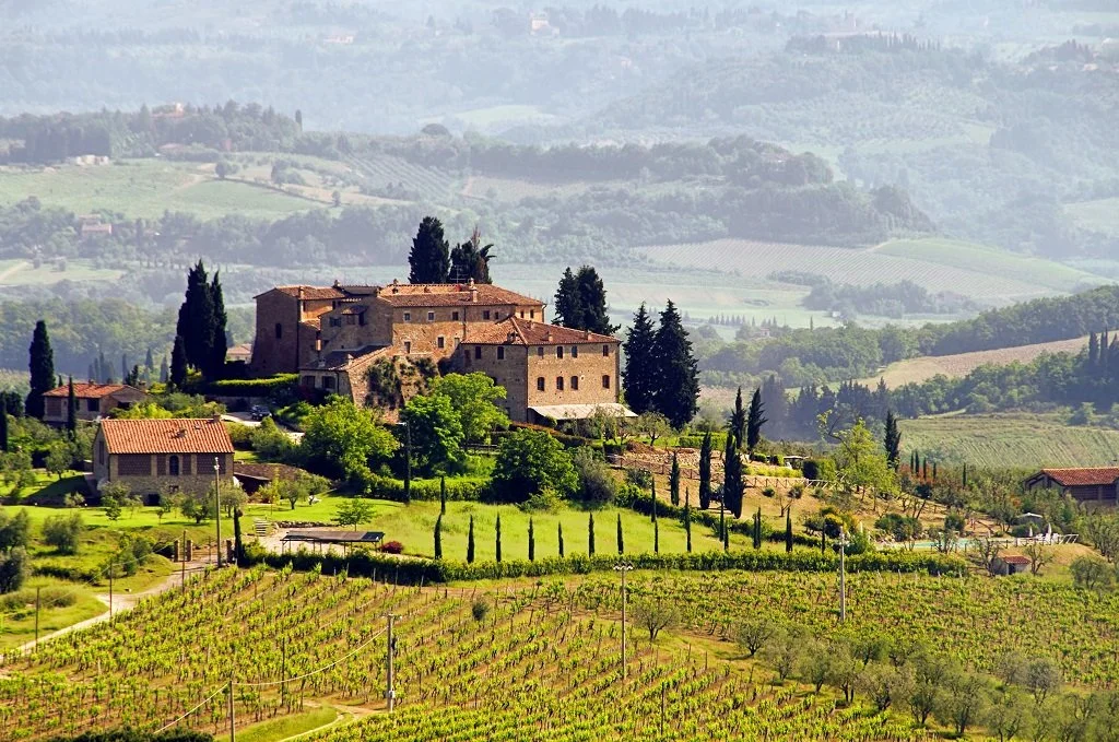 A traditional stone villa and winery estate nestled in the rolling green hills and vineyards of the Tuscany region in Italy.