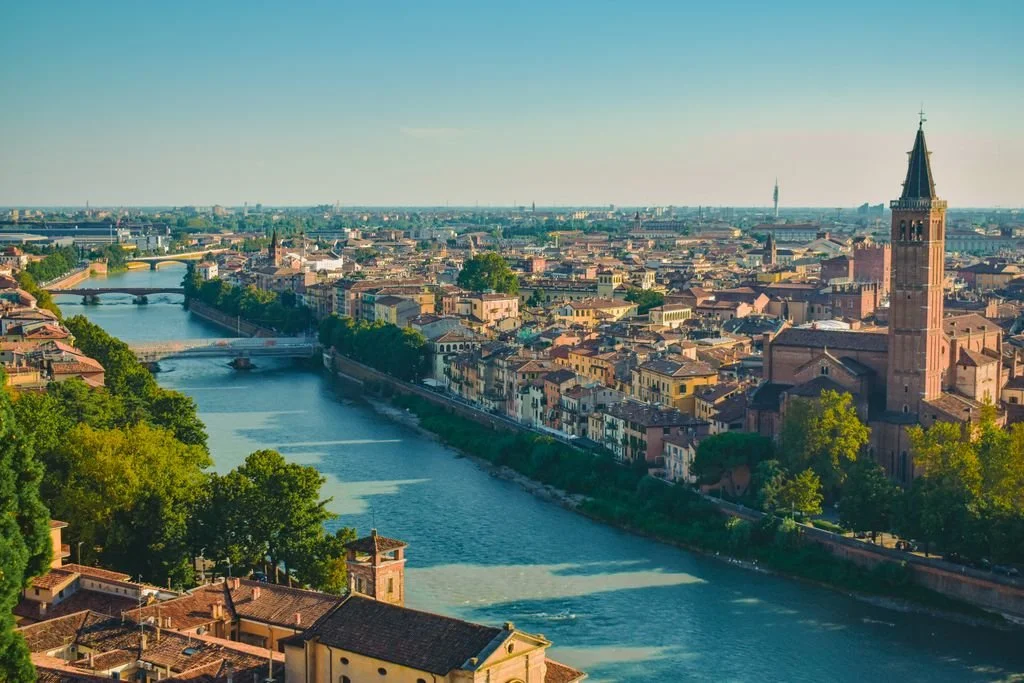 Panoramic view of the historic city center of Verona, Italy, featuring the winding Adige River and the prominent brick bell tower Basilica of Santa Anastasia.