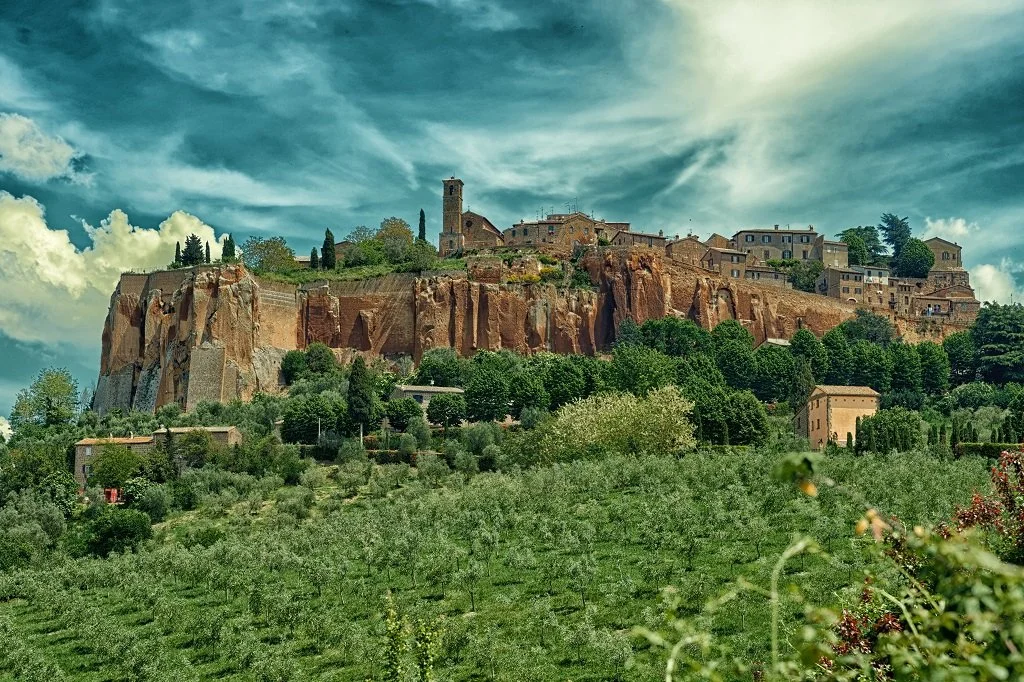 A hillside village with terraced houses atop large rocky cliffs, surrounded by lush greenery and a cloudy sky.