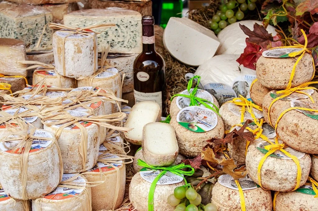 A display of various cheeses, grapes, and a bottle of wine on a market stall.