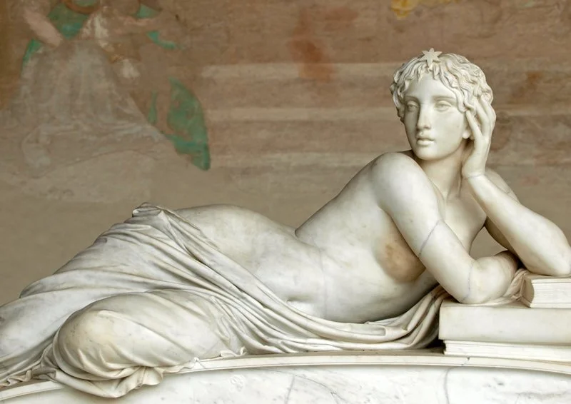 Marble sculpture of a reclining woman with a book, resting her head on her hand, with detailed drapery and naturalistic features.