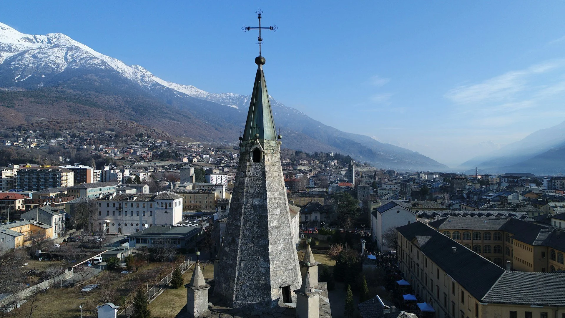 Bell tower of the Collegiata dei Santi Pietro e Orso (Collegiate Church of Saint Ursus) in Aosta, Italy, snow-capped Alps in the background.