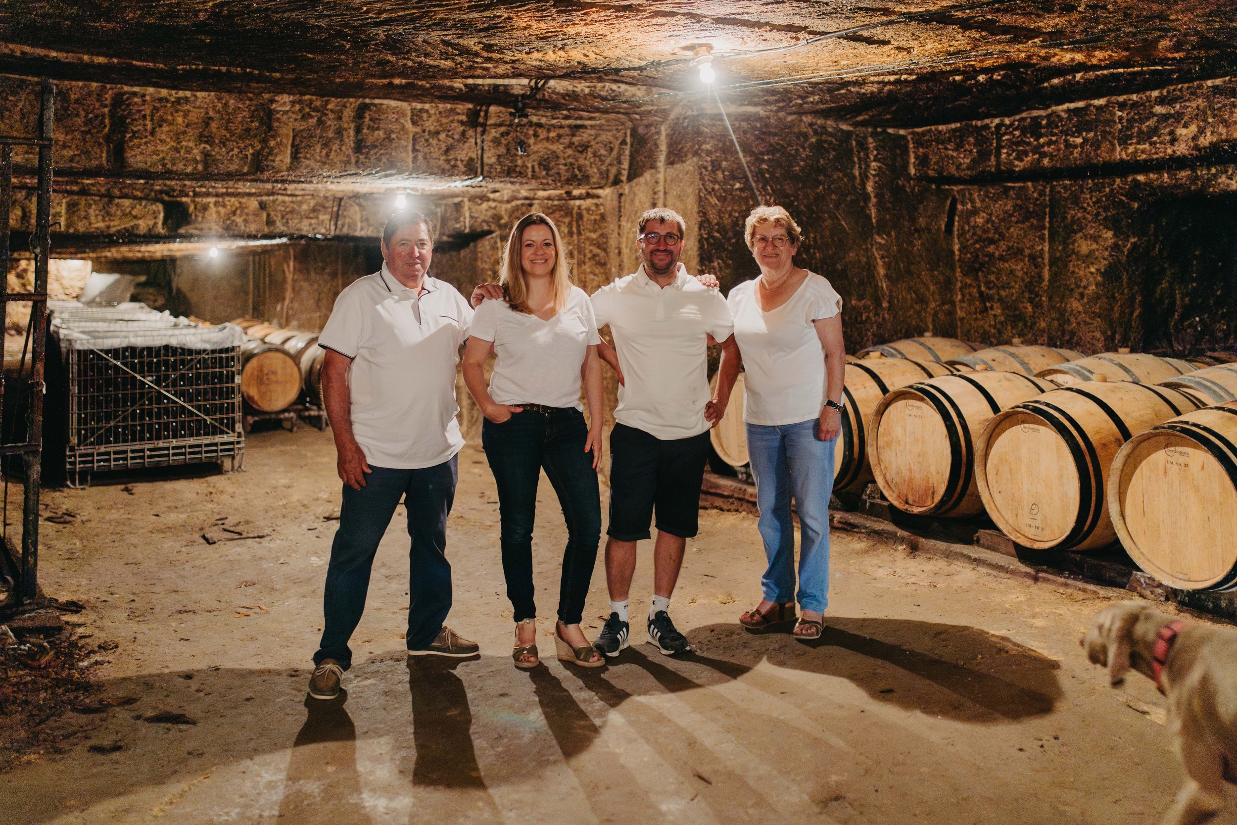Quatre personnes posent dans une cave à vin, entourées de barriques en bois.