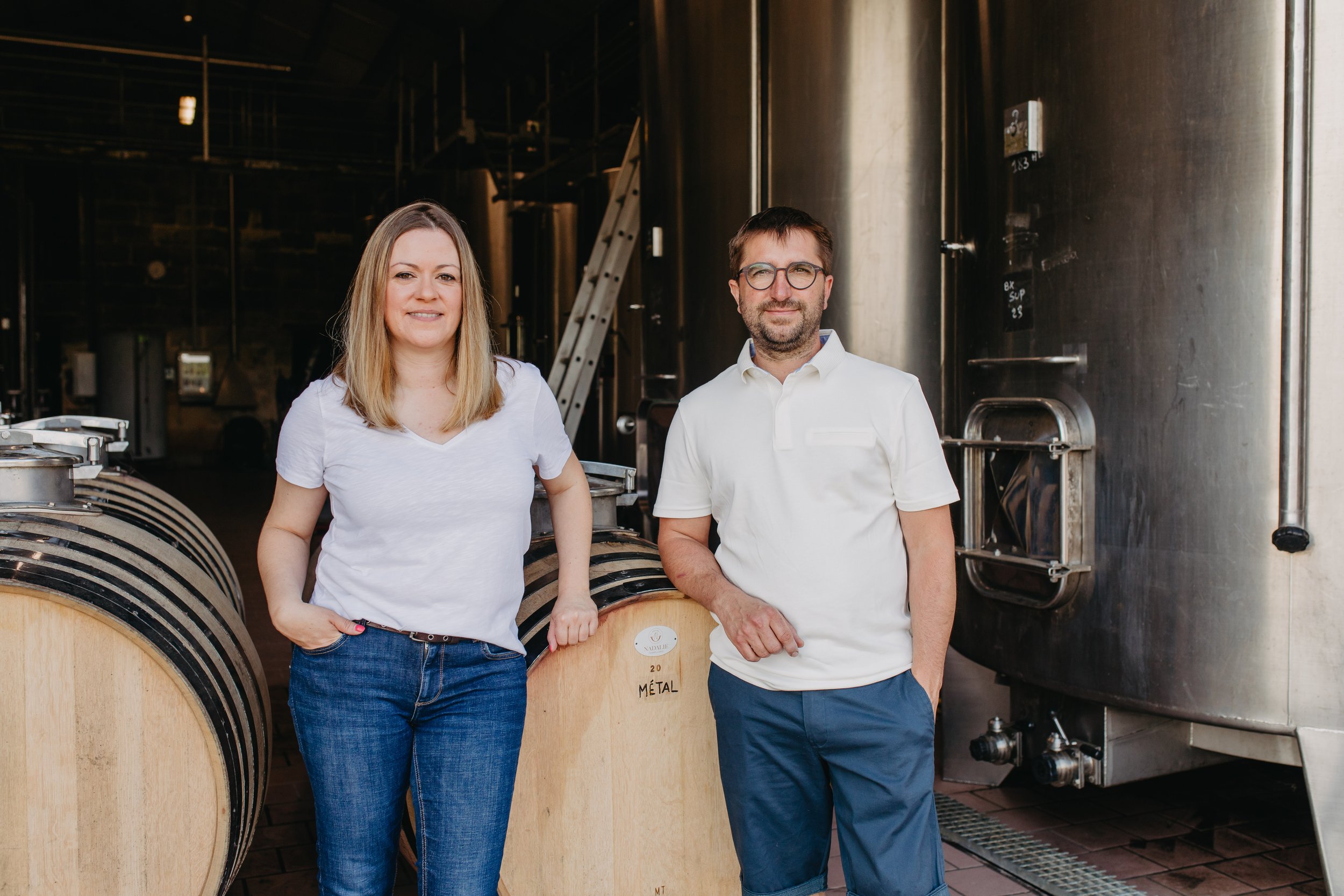 Deux personnes devant des tonneaux et équipements de distillerie.