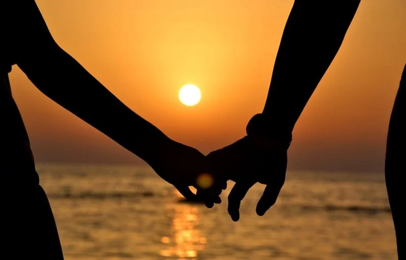 Two people holding hands at sunset over the ocean.