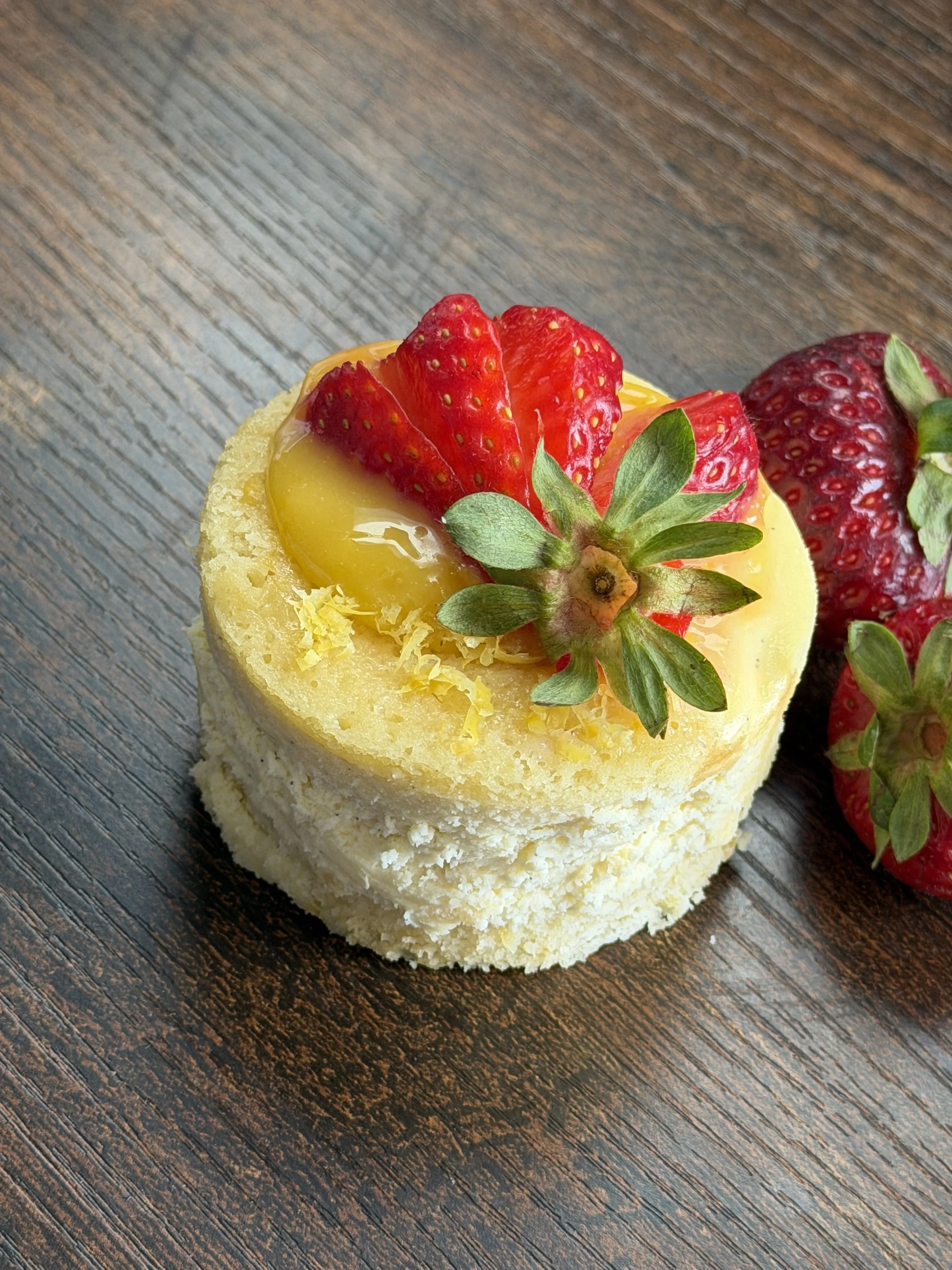Lemon Cake Cheesecake. Layers of tender lemon cake and creamy vanilla bean cheesecake. Garnish Lemon Curd, Fresh Strawberry and a sprinkle of Lemon Zest.