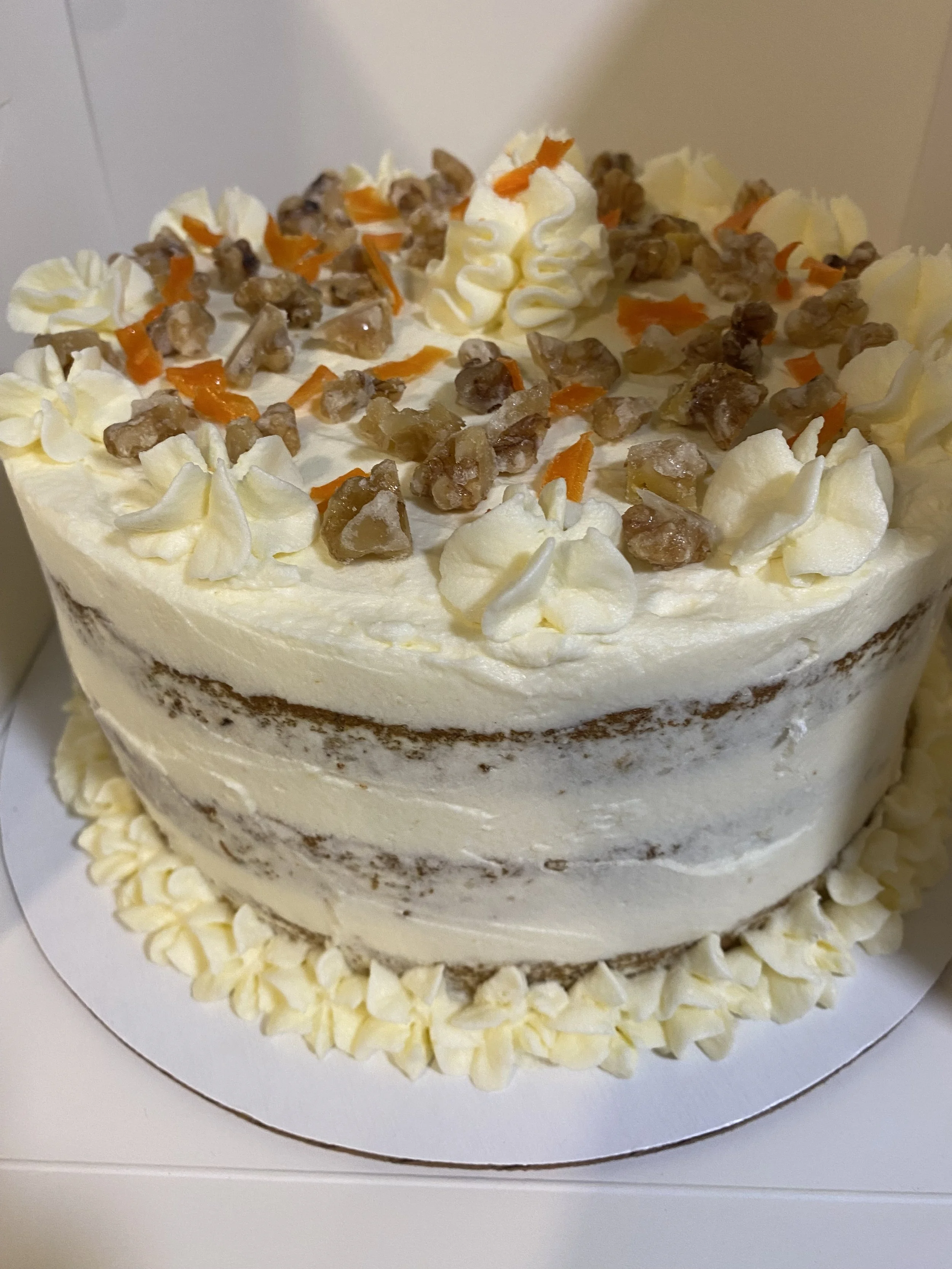 Carrot Cake (Semi-Naked Frosting - light frosting around cake layers).  Cake layers filled with Cream Cheese Italian  Meringue Buttercream and Semi-Naked Frosting.   Garnished with candied walnuts and carrots and frosting piped open stars on top of c