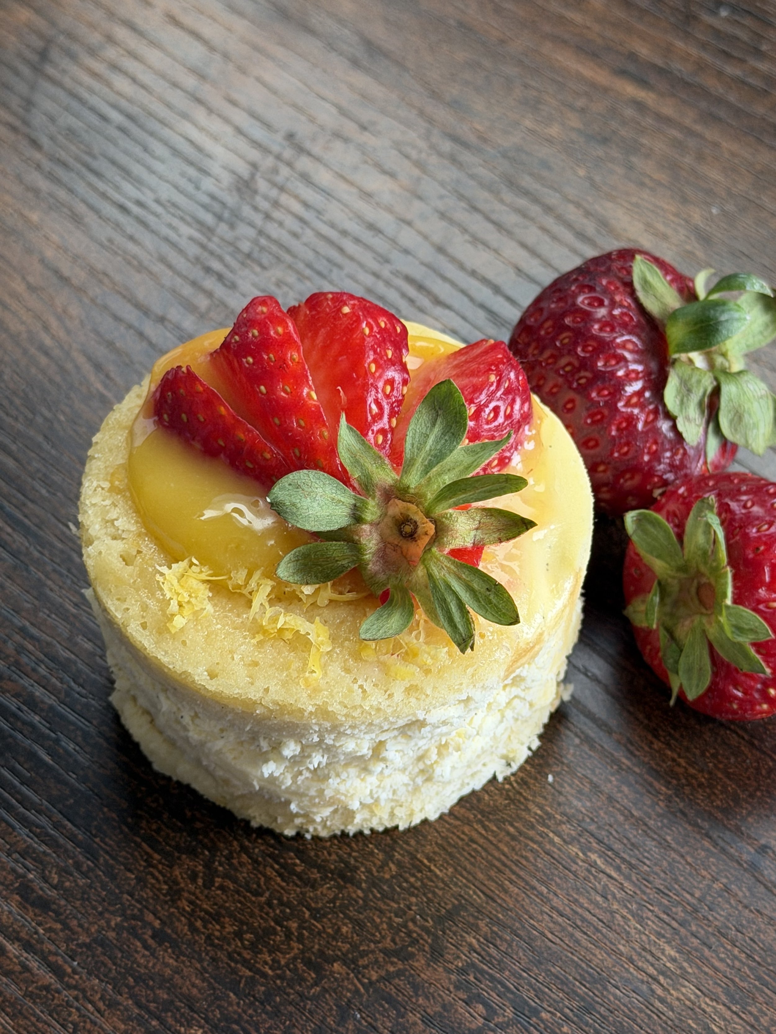 Individual Tall Lemon Cake Cheesecake.  Finished with Lemon Curd, Fresh Strawberry, and Lemon Zest garnish.