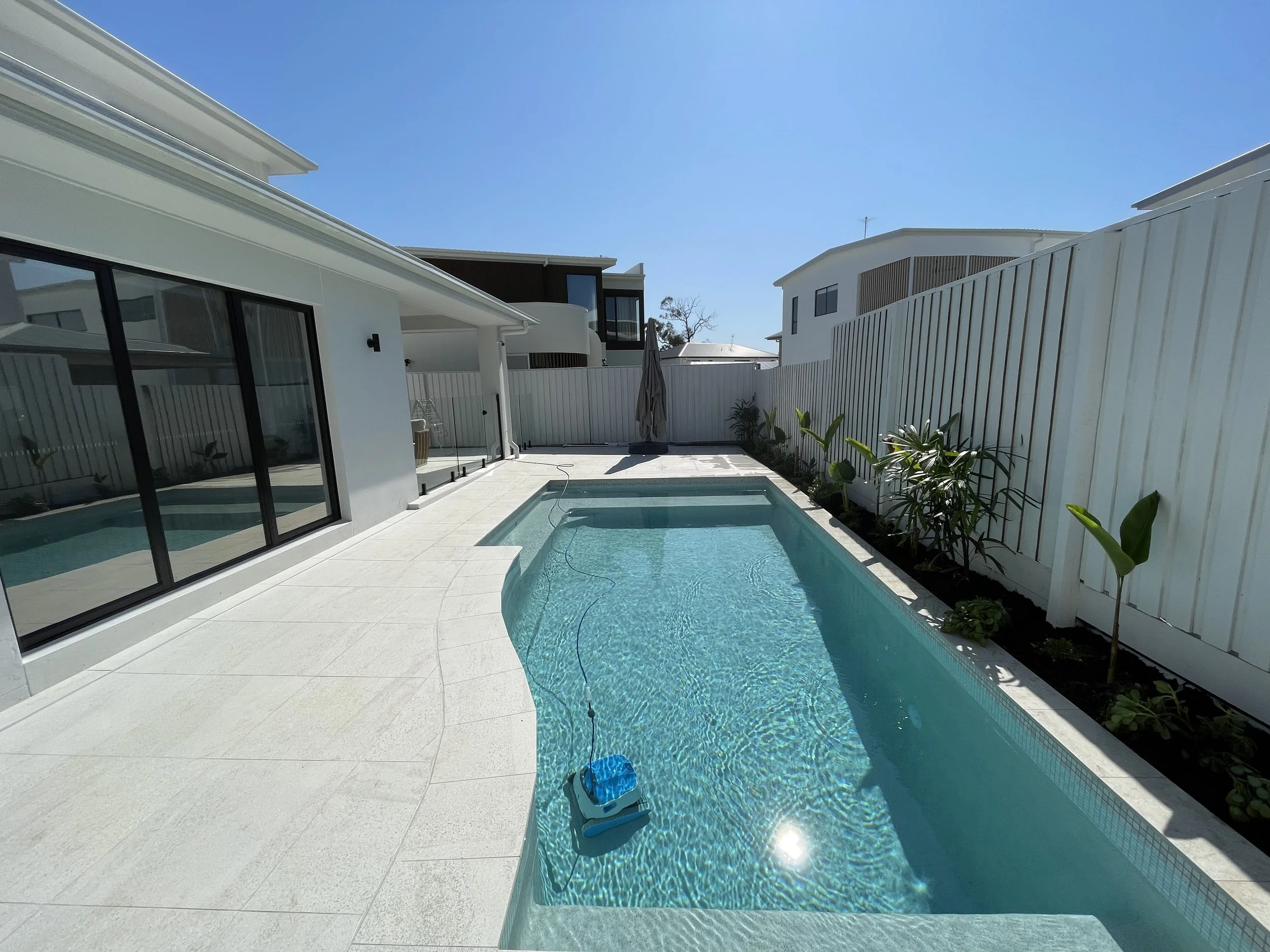 Modern backyard with a swimming pool, outdoor seating area with wooden posts, and a covered pavilion at dusk.