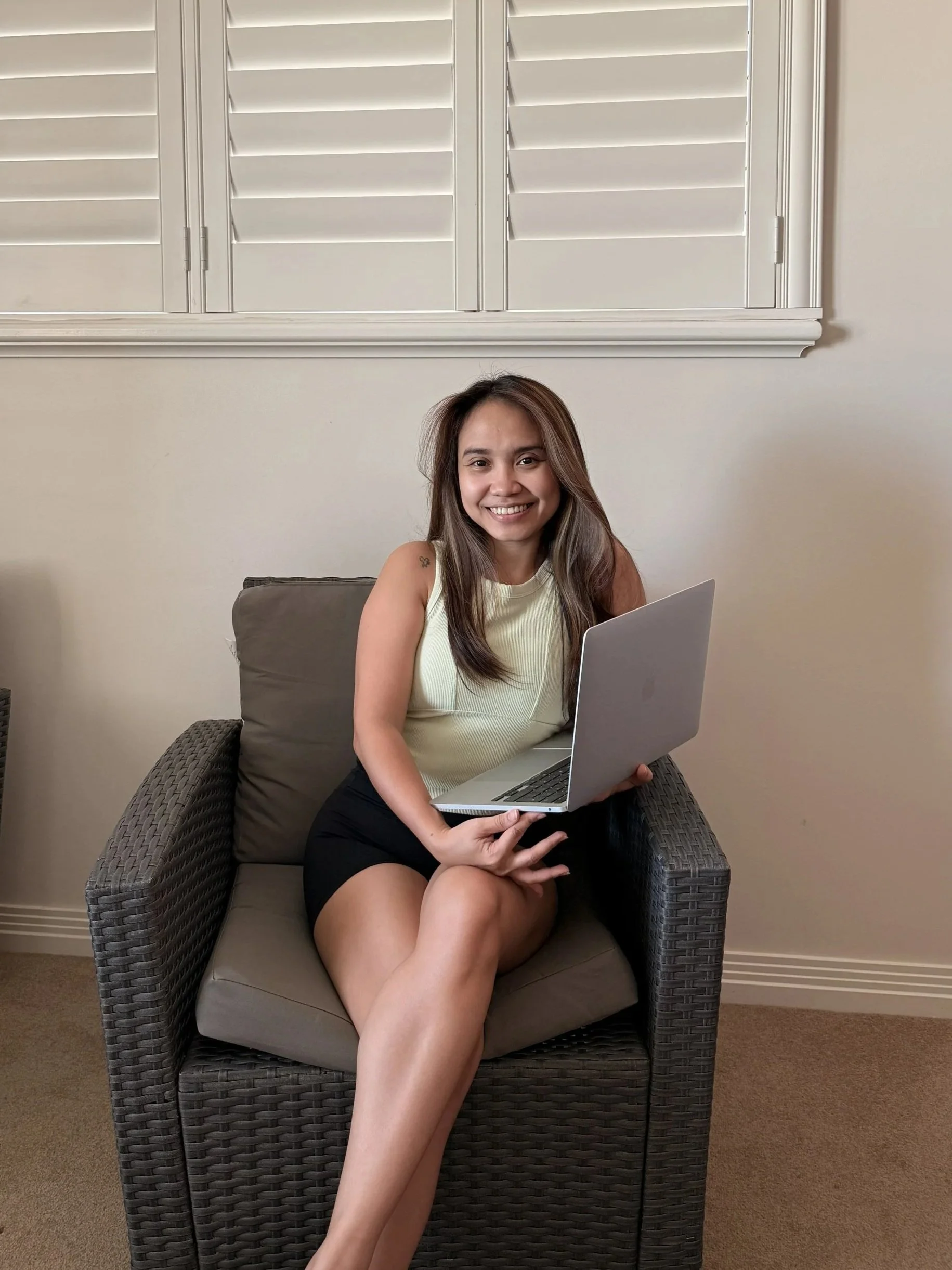 An admin assistant sitting on an armchair holding a laptop, smiling, in a gym.