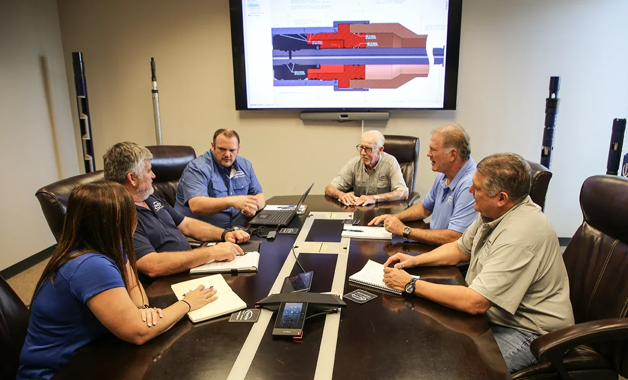 Six people in a meeting room with a large screen showing a technical diagram.